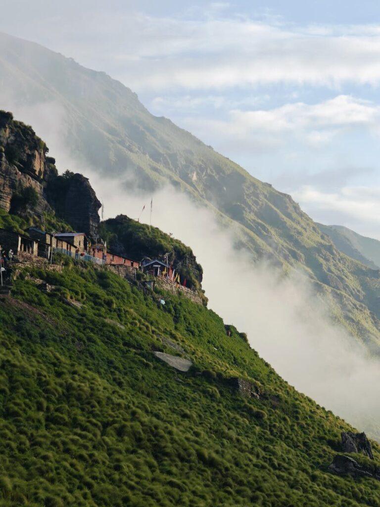 A tranquil mountain village nestled on a grassy slope amidst misty clouds.