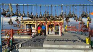 Colorful temple adorned with bells in the Himalayas, featuring visitors in vibrant clothing.