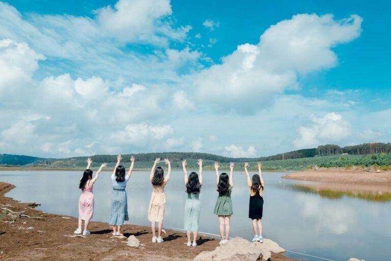 A group of young women enjoy a summer day by a tranquil lake, expressing joy and freedom.