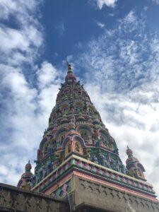 Vibrant tower of a Hindu temple reaching into a partly cloudy blue sky, showcasing intricate architecture.