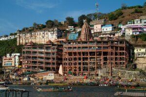 A vibrant riverside scene featuring a majestic temple surrounded by colorful hillside buildings in India.